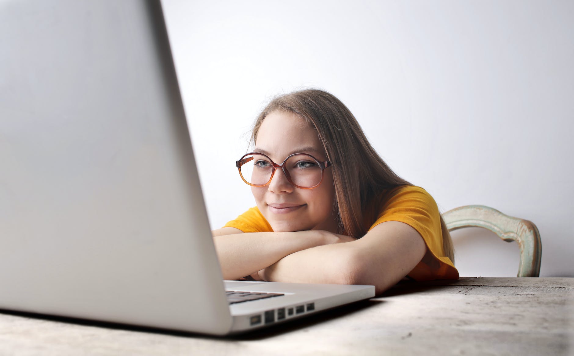 photo of smiling woman in a yellow shirt watching her laptop